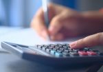 Mãos usam uma calculadora e fazem anotações em um caderno, representando o planejamento do orçamento familiar.
