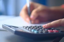 Mãos usam uma calculadora e fazem anotações em um caderno, representando o planejamento do orçamento familiar.