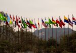 Diversas bandeiras nacionais hasteadas diante de uma paisagem montanhosa, simbolizando a cooperação internacional.