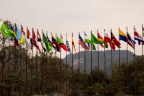 Diversas bandeiras nacionais hasteadas diante de uma paisagem montanhosa, simbolizando a cooperação internacional.
