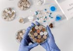 Cientista usando luvas examina amostras de solo em placas de Petri sobre uma bancada branca.