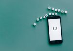 Smartphone exibindo a palavra “PAY”, cercado por dados sobre uma superfície azul.