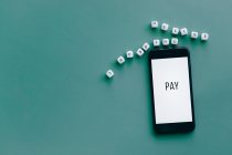 Smartphone exibindo a palavra “PAY”, cercado por dados sobre uma superfície azul.