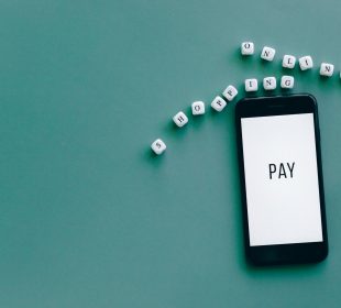 Smartphone exibindo a palavra “PAY”, cercado por dados sobre uma superfície azul.