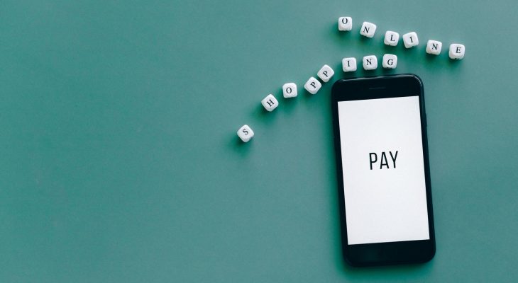 Smartphone exibindo a palavra “PAY”, cercado por dados sobre uma superfície azul.
