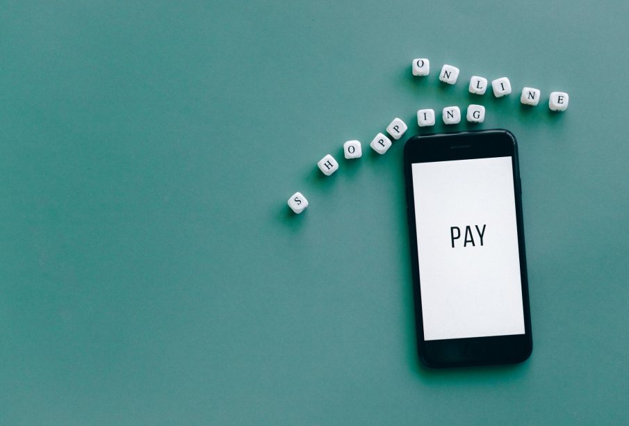 Smartphone exibindo a palavra “PAY”, cercado por dados sobre uma superfície azul.